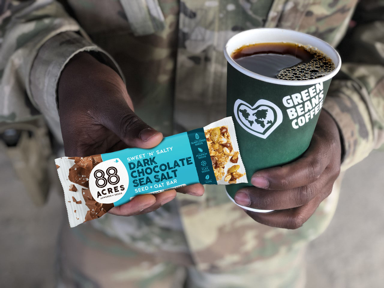 Service Member in uniform holding a Green Bean Coffee cup and 88 Acres snack bar